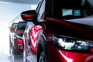 Red SUV car parked in modern showroom. New and luxury SUV compact car. Car dealership concept. Automotive industry. Automobile leasing business. Front view of red shiny car parked in showroom. photo