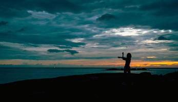 Silhouette woman workout in the morning at stone beach with beautiful sunrise sky. Fit woman stretching body before workout. Exercise for healthy lifestyle. Out door workout. Nature landscape. Freedom photo