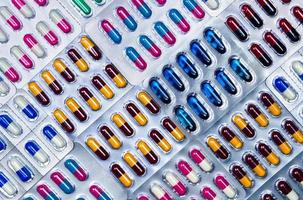 Top view of capsule pills in blister pack. Pharmaceutical industry. Pharmaceutical manufacturing industry concept. Capsule pills production. Full frame shot of blue, pink, yellow, red, black capsules. photo