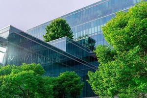 Eco-friendly building with vertical garden in modern city. Green tree forest on sustainable glass building. Energy-saving architecture with vertical garden. Office building with green environment. photo