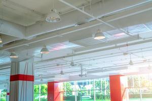 Air duct, air conditioner pipe, fire sprinkler and wiring system. Building interior. Ceiling lamp light with opened light. Interior architecture. Glass wall building and exterior garden with sunlight.