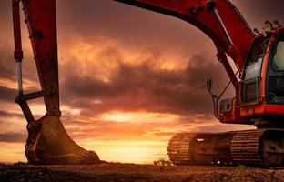 Backhoe parked at construction site after digging soil. Bulldozer on sunset sky and clouds background. Digger after work. Earth moving machine at construction site at dusk. Digger with old bucket. photo