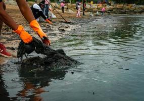 adultos y niños voluntarios recogiendo basura en la playa del mar. contaminación del medio ambiente de la playa. ordenar la basura en la playa. la gente usa guantes naranjas saca plástico en el barro de la playa del mar. foto