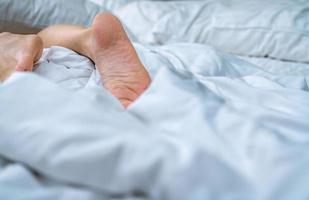 Cierra los pies descalzos de la mujer en la cama sobre una manta blanca y una sábana en el dormitorio de la casa o del hotel. concepto de dormir y relajarse. mañana perezosa. descalzo de mujer acostada en cama blanca y edredón. foto