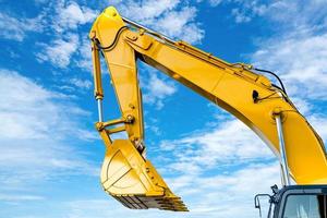 Yellow backhoe with hydraulic piston arm against blue sky. Heavy machine for excavation in construction site. Hydraulic machinery. Huge bulldozer. Heavy machine industry. Mechanical engineering. photo