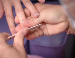 Woman receiving fingernail manicure service by professional manicurist at nail salon. Beautician file nail manicure at nail and spa salon. Hand care and fingernail treatment at nail salon. photo