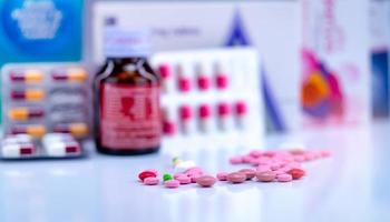 Tablets and capsule pills on blurred drug bottle, capsule in blister pack and paper box package of medicine. Pink and red tablets and green-yellow capsule on pharmacy counter. Pharmaceutical industry. photo