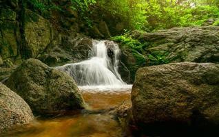 Beautiful waterfall in jungle. Waterfall in tropical forest with green tree and sunlight. Waterfall is flowing in jungle. Nature background. Rock or stone at waterfall. Green season travel in Thailand photo