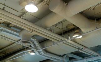 Air duct, wiring and plumbing in the mall. Air conditioner pipe, wiring pipe, and plumbing pipe system. Building interior concept. Ceiling lamp light with opened light. Interior architecture concept. photo