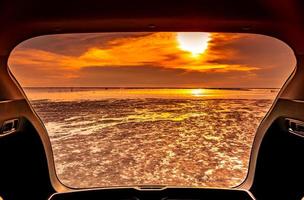 Beautiful sea view from inside car trunk. Sea view with orange sky and clouds in sunset time at the beach. Freedom summer travel with road trip on vacation concept. Romantic view in the evening. photo