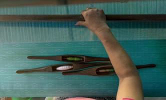 Woman working on weaving machine for weave handmade fabric. Textile weaving. Weaving using traditional hand weaving loom on cotton strands. Textile or cloth production in Thailand. Asian culture. photo