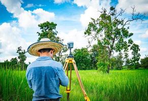 Asian smart engineer or surveyor working on controller screen for surveying land in rice field, Thailand. GPS surveying instrument. GPS equipment. Land survey for map. People work in good environment. photo