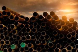 Pile of old rusty round metal industrial pipe. Steel pipe stack during sunset. Industrial material. Metal corrosion. Stack of round rusty tube abstract background. Old iron pipe warehouse of factory photo