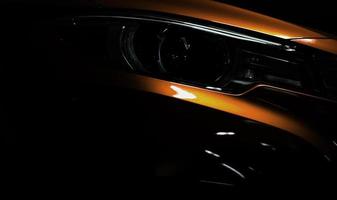 Closeup headlight of shiny orange luxury SUV compact car. Elegant electric car technology and business concept. Hybrid auto and automotive. Car parked in showroom or motor show. Car dealership. photo
