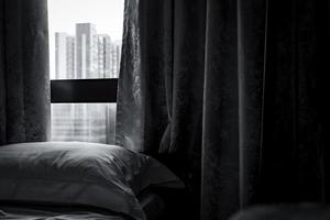 cama cómoda blanca y almohada suave en un dormitorio moderno. cama cerca de la ventana y cortina en el hotel. sábana de lino y funda de almohada. diseño de interiores de dormitorio. escena en blanco y negro del dormitorio de lujo en el hotel. foto