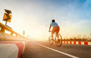 Blur back view of a man wear helmet ride a bicycle for exercise. Curve road traffic sign with people cycling bike on the road. Outdoor activity in summer. Healthy lifestyle.  Sport and activity. photo