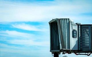 Jet bridge after commercial airline take off at the airport against blue sky and white clouds. Aircraft passenger boarding bridge docked. Departure flight of international airline. Empty jet bridge. photo