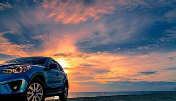 Blue compact SUV car with sport and modern design parked by beach at sunset. Hybrid and electric car technology. Car parking space. Automotive industry. Car care business background. Beautiful sky. photo
