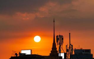 hermoso cielo al atardecer sobre la ciudad. edificio del templo de silueta y torre de telecomunicaciones. antena sobre fondo de cielo al atardecer. poste de radio y satélite. cielo rojo del atardecer en verano. cielo de verano tropical. foto