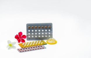 Contraceptive pills or birth control pills and condom with pink and white flowers on white background with copy space. Hormone and condom for contraception.  Protect unplanned pregnancy concept. photo