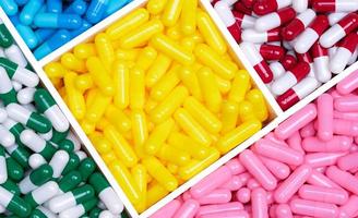 Top view colorful capsule pills in a plastic tray. Yellow, pink, red, green, and blue capsule pills. Antibiotics, vitamins, and supplements capsules. Pharmaceutical industry. Prescription drugs. photo