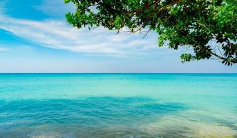 Beautiful tropical paradise beach background. Summer vibes. Summer vacation time background. Ocean waves. Calm, tranquil and relax scene. Emerald green sea water and blue sky and white clouds. Skyline photo