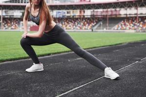 Stretch for the legs. Young blonde warming up on the track in the stadium at daytime photo