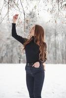 Calm weather. Pretty girl with long hair and in black blouse is in the winter forest photo