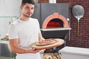 trabajo bien hecho. panadero con camisa blanca con pizza lista para poner en el horno para cocinar foto