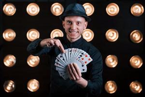 He's gonna guess your card. Magician in black suit standing in the room with special lighting at backstage photo