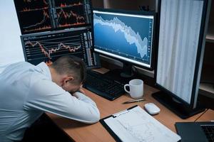Tired of hard day. Man working online in the office with multiple computer screens in index charts photo