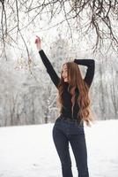 quieren divertirse. linda chica con cabello largo y blusa negra bailando en el bosque de invierno foto