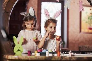 Trying their best. Have happy easter. Two little girls learning how to paint eggs for the holidays photo