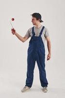 Roller for painting walls. Man in blue uniform stands against white background in the studio photo