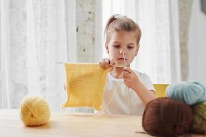 School of art. Kid is knitting at home. Cute little girl sitting near the wooden table is learning some new stuff photo