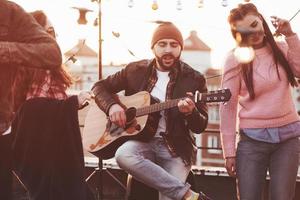 Just feel the music. Friends have fun at rooftop party with decorative colored light bulbs photo