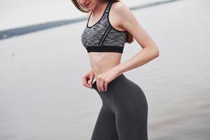 sostiene los pantalones con las manos. foto recortada de una chica fitness posando después de correr por la mañana cerca del lago