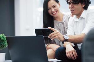 Let's capture these results. Coworkers in a modern office use smartphone to take picture from laptop photo