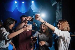 Careful with drinks. Group of young friends smiling and making a toast in the nightclub photo