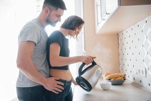 abrazando a la niña. pareja joven en la cocina moderna en casa en su tiempo de fin de semana en la mañana foto