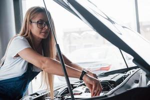 Replacement of a parts. On the lovely job. Car addicted woman repairs black automobile indoors photo