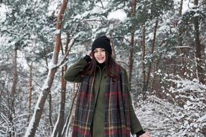 mujer encantadora. una joven alegre con ropa de abrigo da un paseo por el bosque de invierno durante el día foto