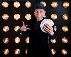 Card tricks in action. Magician in black suit standing in the room with special lighting at backstage photo