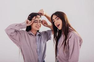 Playng with glasses. Two sisters twins standing and posing in the studio with white background photo