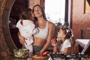 Young mother with kids standing in the kitchen and have some fun photo
