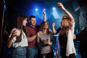 no seas tímido, muestra tus movimientos. gente feliz bailando en el club nocturno de lujo junto con diferentes bebidas en sus manos foto