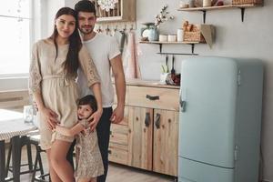 todos se abrazan. linda foto familiar de madre embarazada, padre y su hija. de pie en la cocina