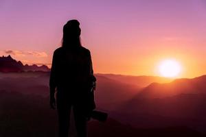 Back view of young hipster photographer holding the camera with sunset on mountain natural background. photo