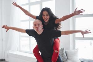 Playful couple in black and red clothes having fun in the white room in daytime photo