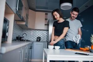 Man hugs his girlfriend. Young couple in the modern kitchen at home at their weekend in the morning time photo